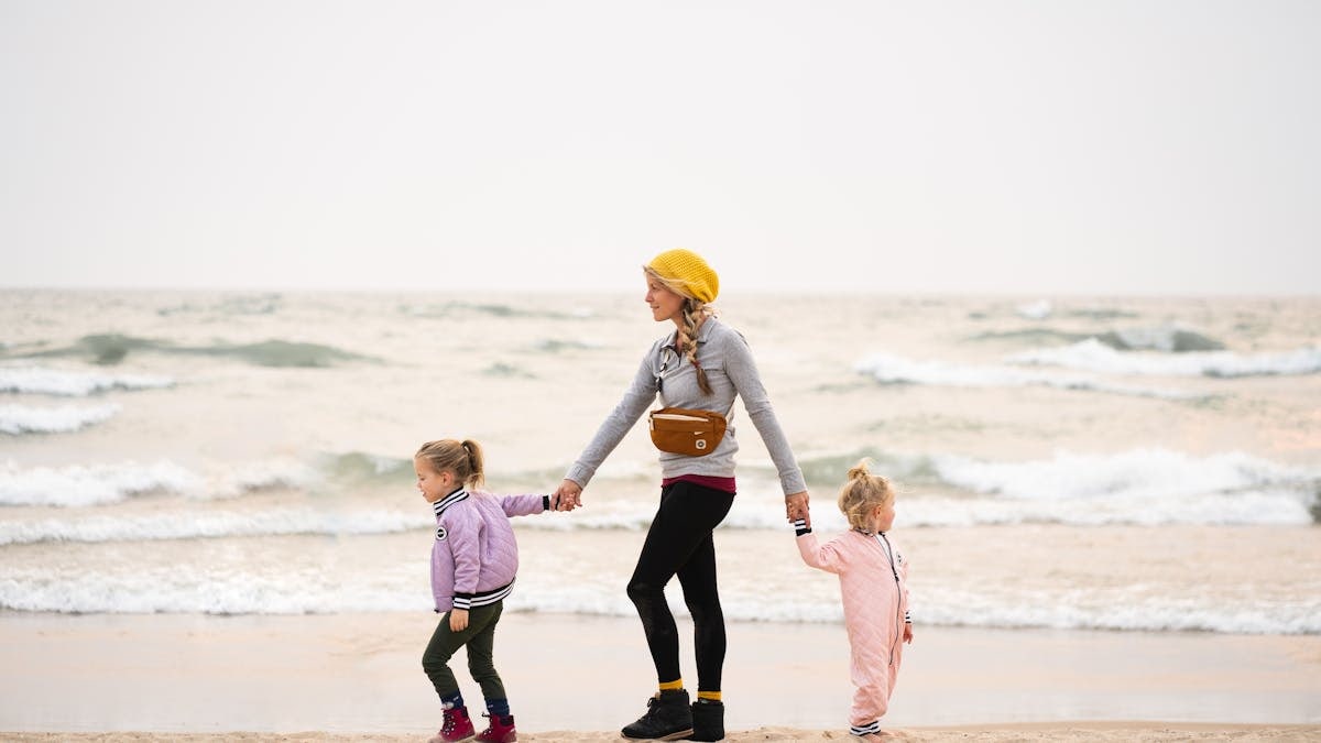 A mother walks hand-in-hand with two young daughters on Grand Haven Beach, Michigan.
