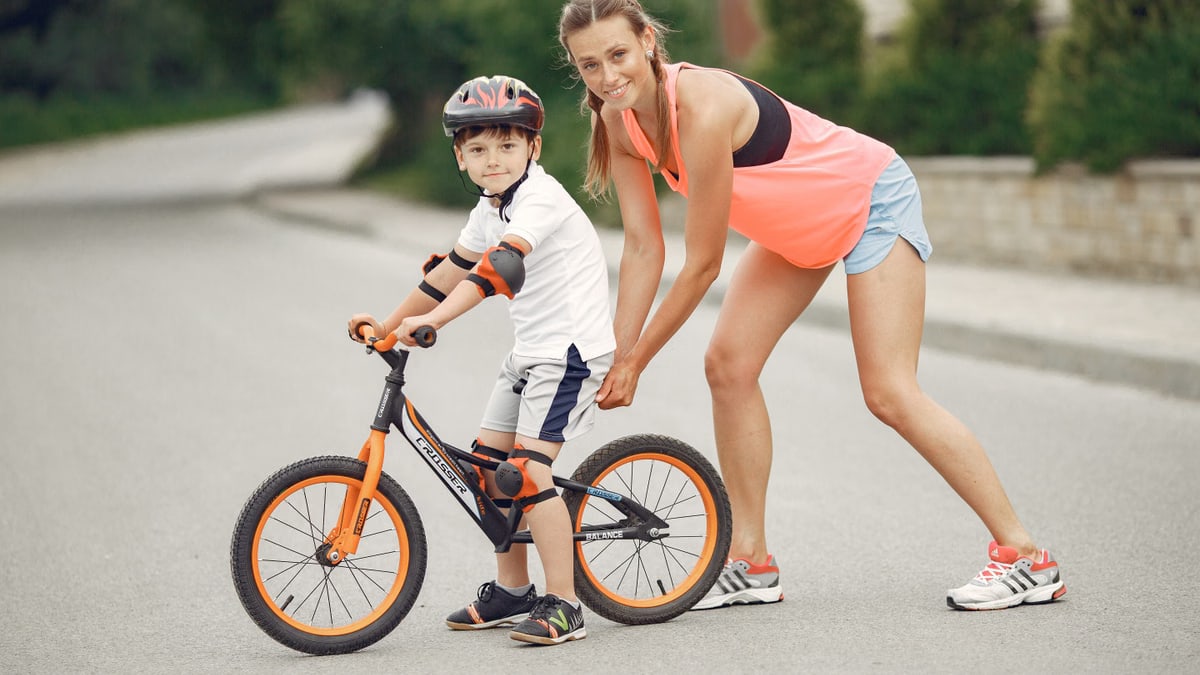 Mother helping her son ride a bicycle in a sunny outdoor setting. Bonding and learning experience.